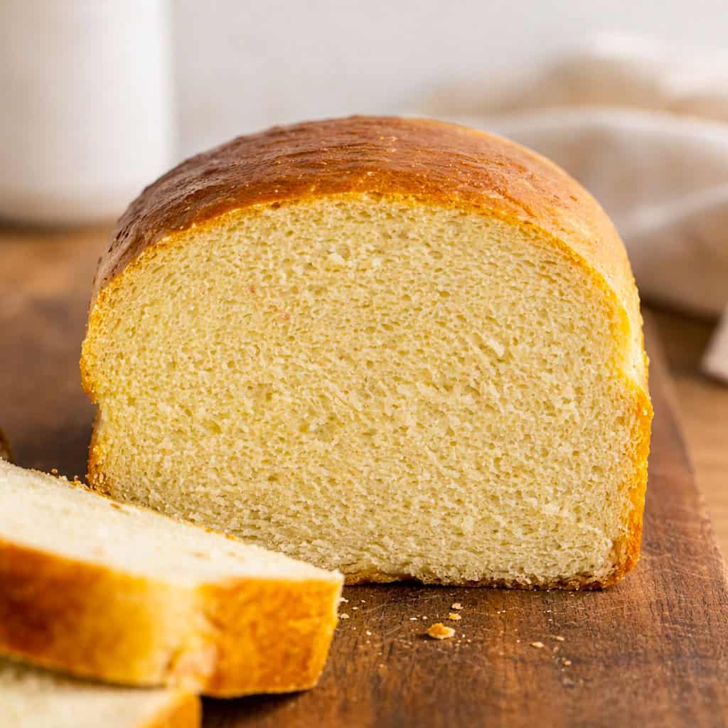 Nothing compares to Hearth Bread, freshly baked surrounded by family. It is an easy recipe that makes two loaves and tastes delicious all on its own! Loaf of Hearth Bread that has been cut with slices laying in front.