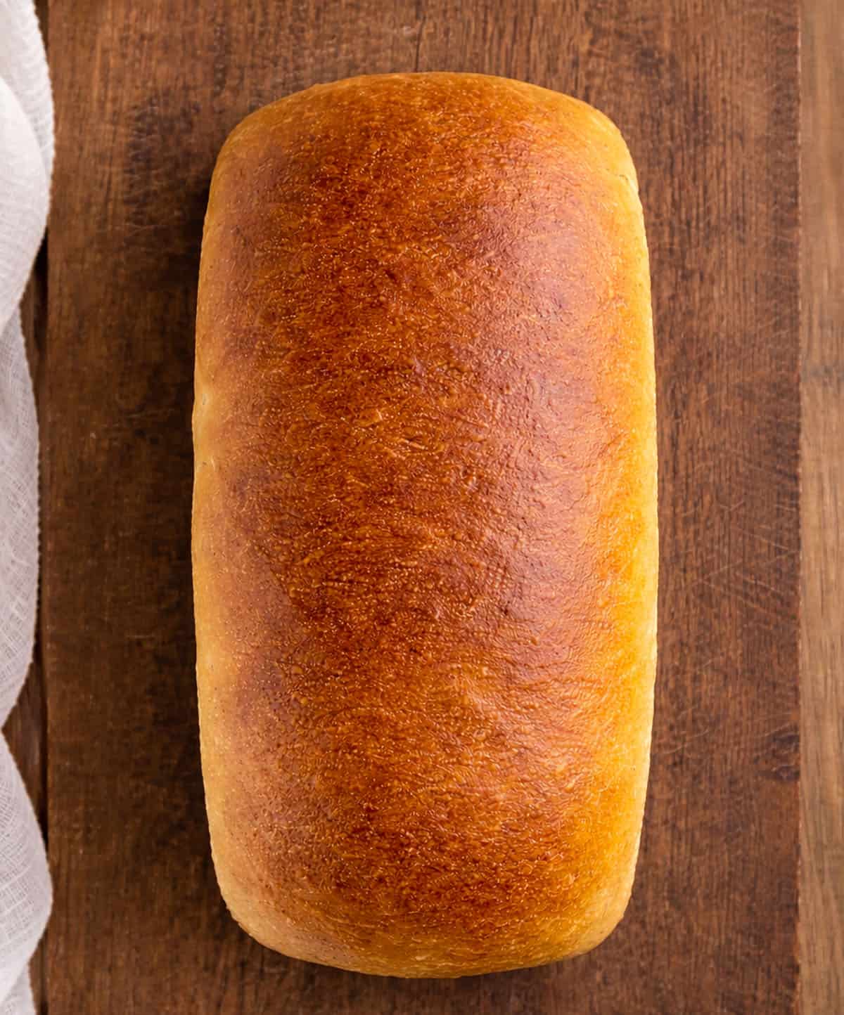Nothing compares to Hearth Bread, freshly baked surrounded by family. It is an easy recipe that makes two loaves and tastes delicious all on its own! Whole loaf of Hearth Bread on a wooden table.