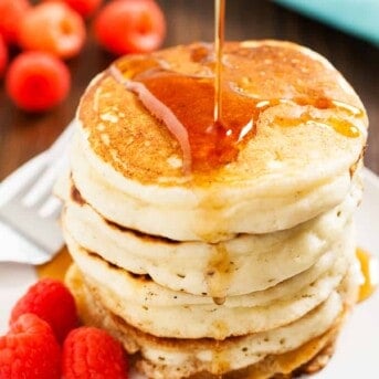 A sweet stack of buttermilk pancakes piled high and syrup being poured over top