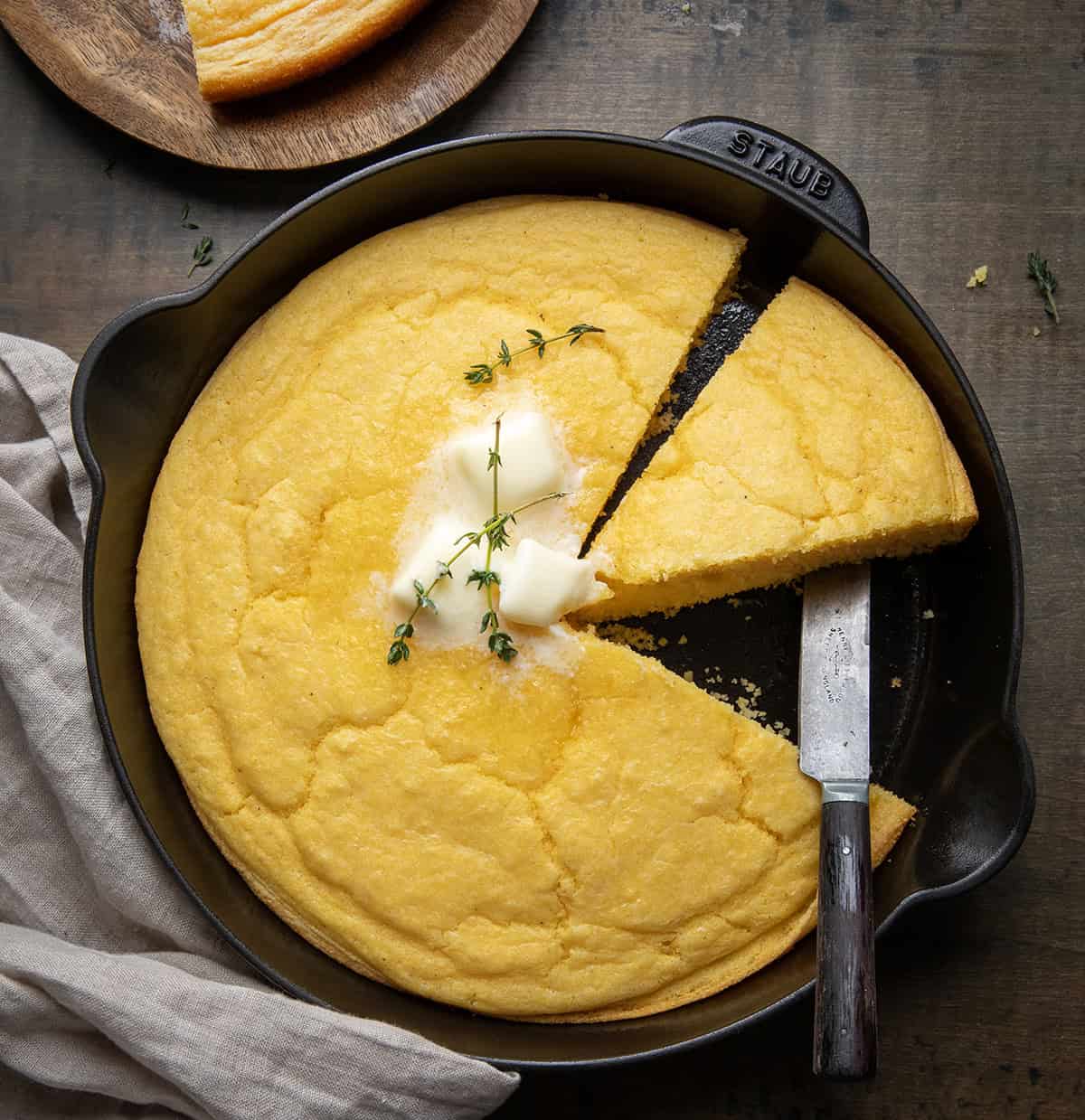 Skillet of Country Homestyle Cornbread on a wooden table from overhead with a few pieces cut out.