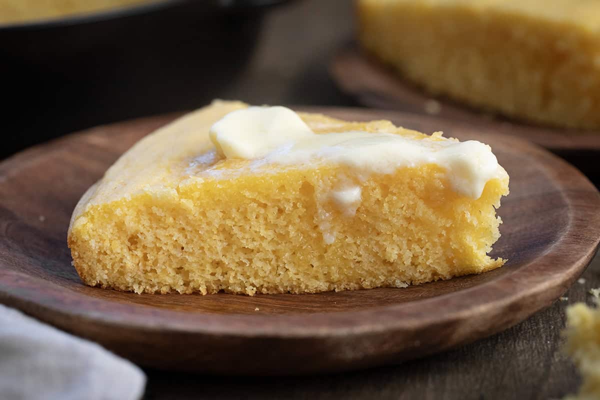 Piece of Country Homestyle Cornbread on a wooden plate with melting butter.