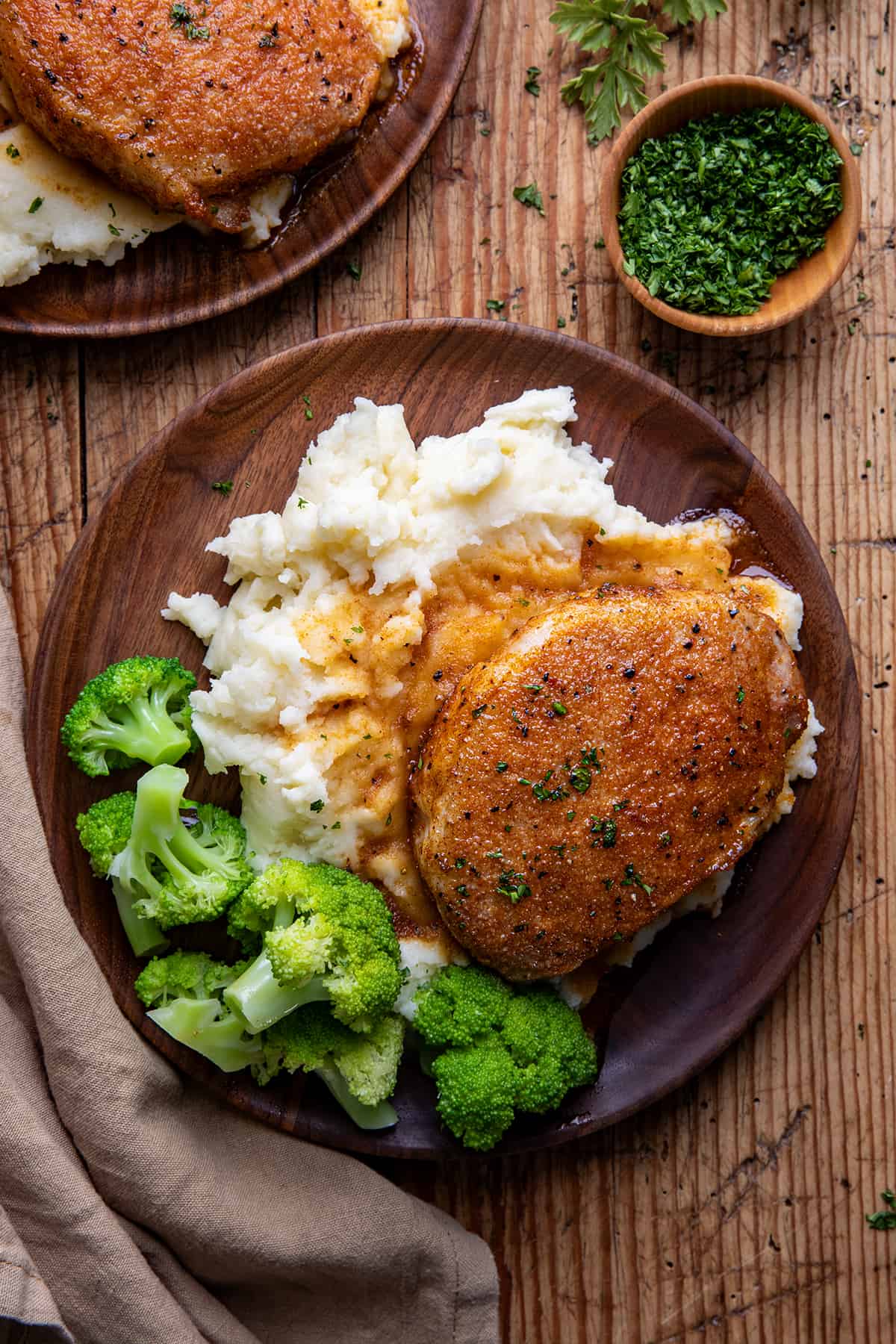 Baked Pork Chops on a bed of mashed potatoes and broccoli on a wooden table.