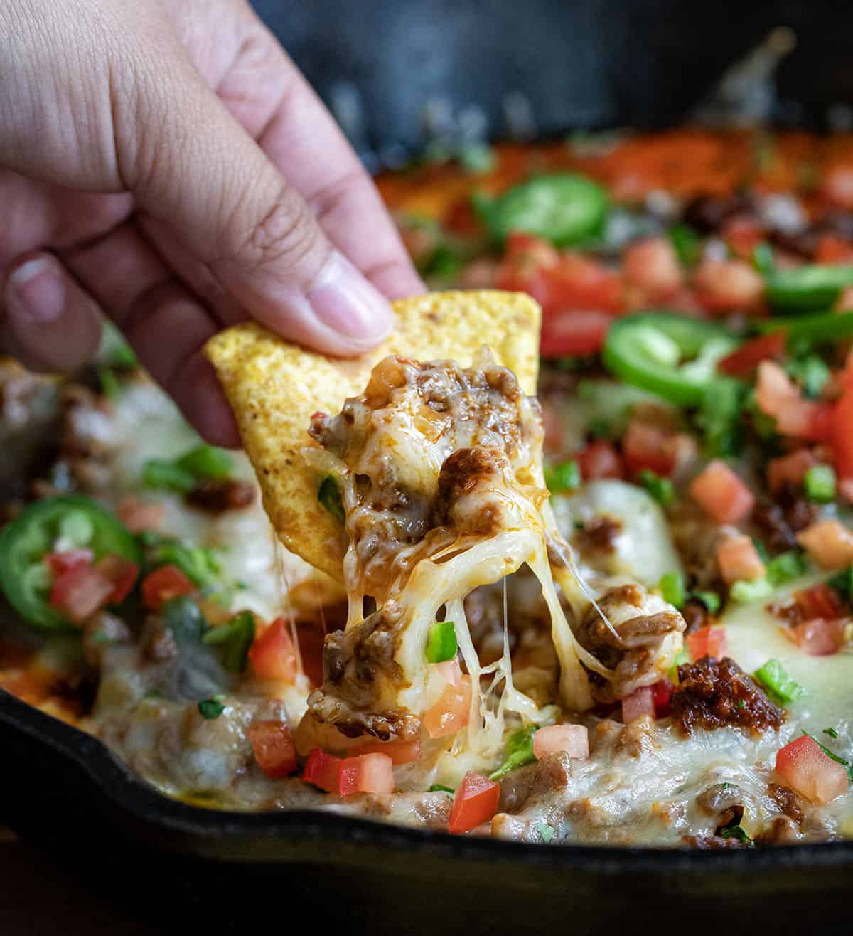 Hand dipping a chip into Queso Fundido.