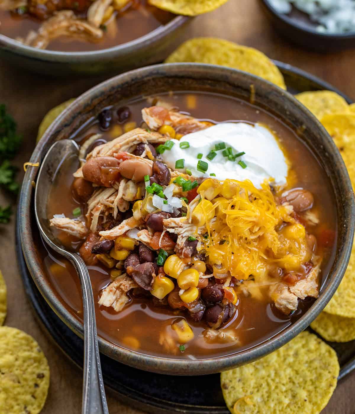 Close up of a bowl of Slow Cooker Chicken Taco Soup with a spoon in it on a wooden table.