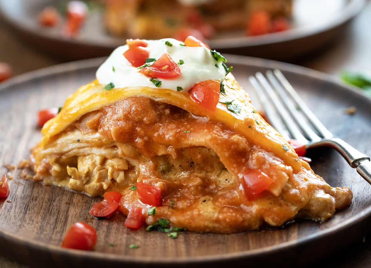 Try this delicious Chicken Tortilla Casserole recipe with layers of tender chicken, creamy cheese, and flavorful enchilada sauce! Piece of Chicken Tortilla Casserole on a wooden table close up.