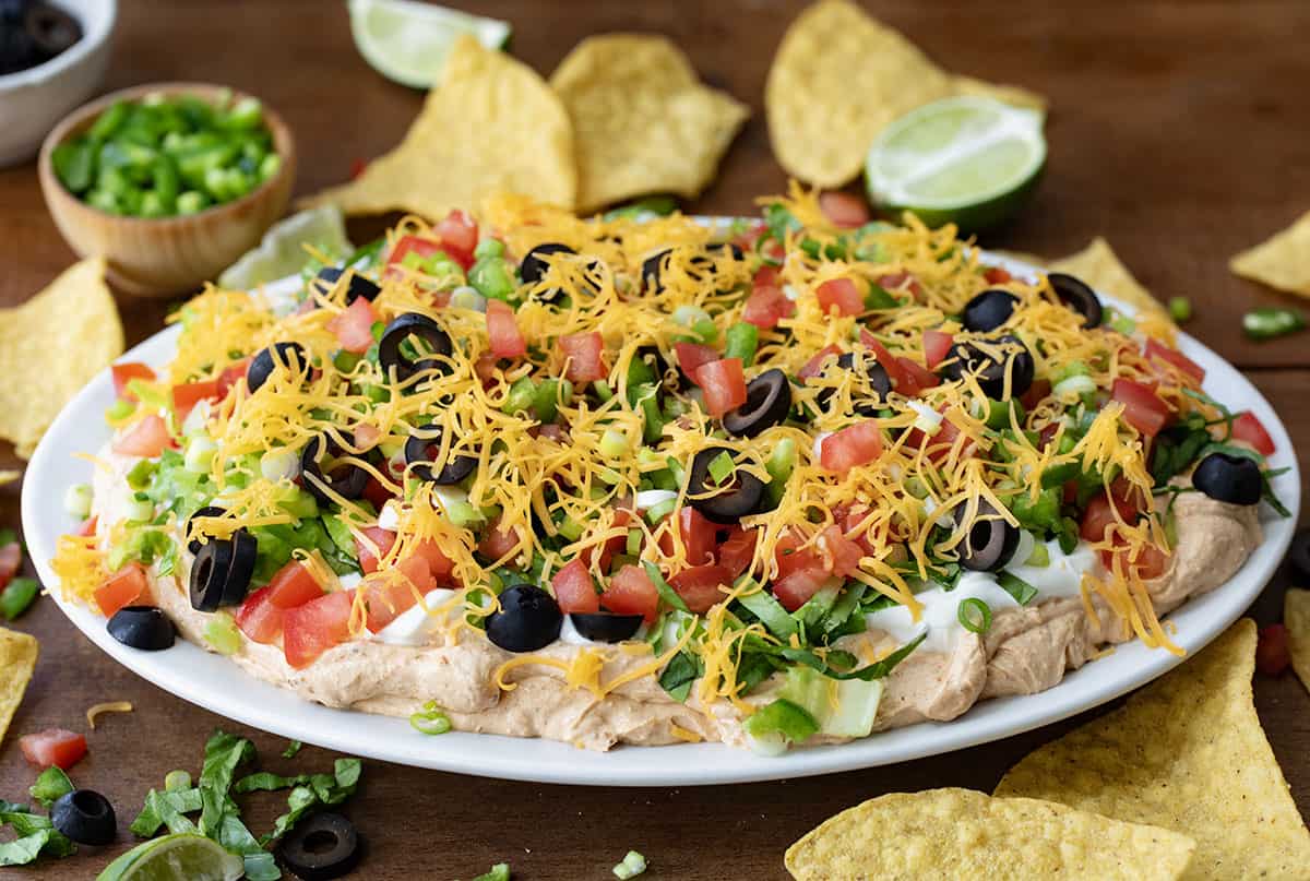 Plate of Taco Dip on a wooden table with chips and limes around.