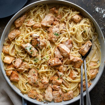 Skillet of Creamy Chicken Pasta on Dark Table with Spoons in the Skillet from Overhead.