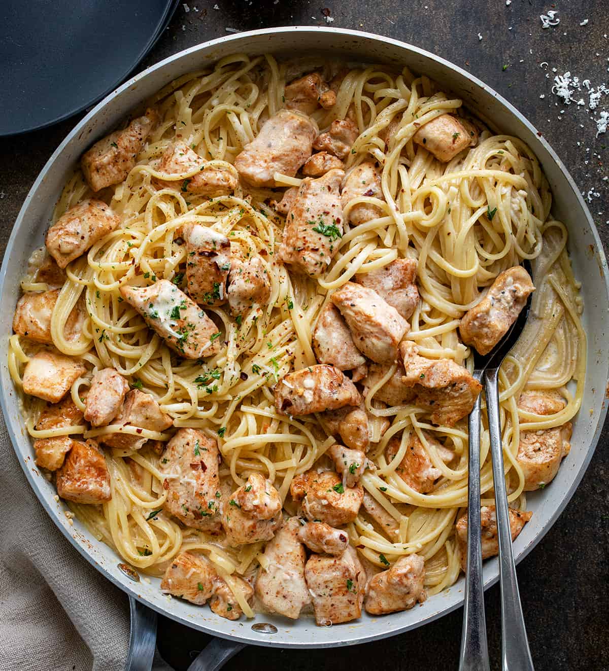 Skillet of Creamy Chicken Pasta on Dark Table with Spoons in the Skillet from Overhead.