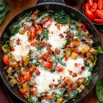 Skillet of Breakfast Skillet Spinach and Eggs on a wooden table from overhead.