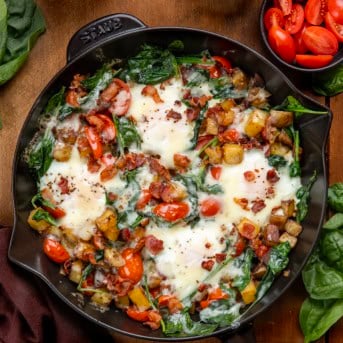 Skillet of Breakfast Skillet Spinach and Eggs on a wooden table from overhead.