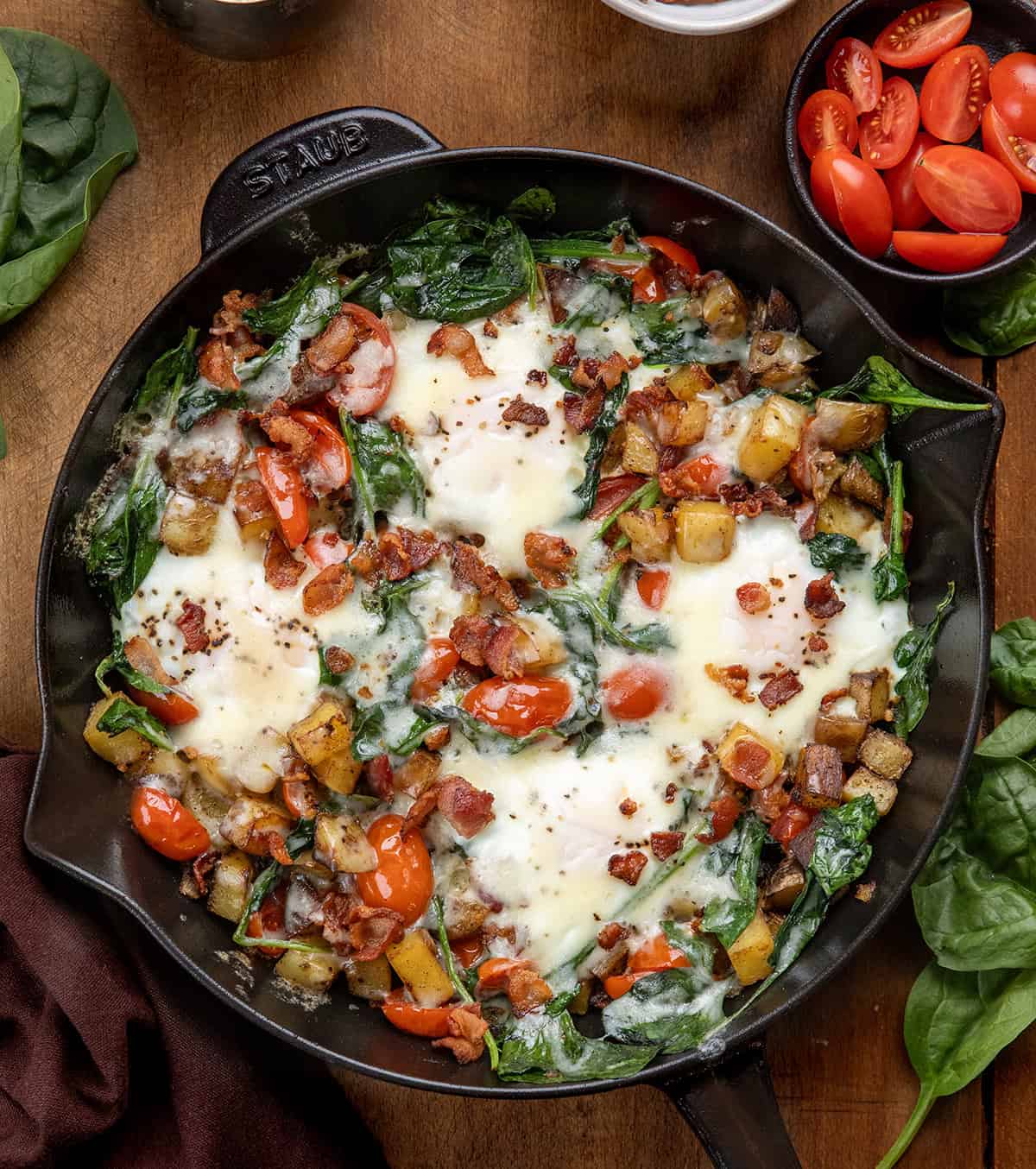 Skillet of Breakfast Skillet Spinach and Eggs on a wooden table from overhead Skillet of Breakfast Skillet Spinach and Eggs on a wooden table from overhead.