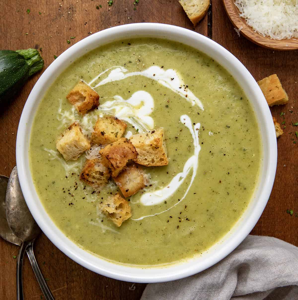 White bowl filled with Zucchini Soup and topped with croutons on a wooden table from overhead.