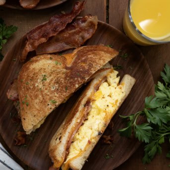 Cut in half Griddle Breakfast Sandwich on a wooden table from overhead with a glass of orange juice.