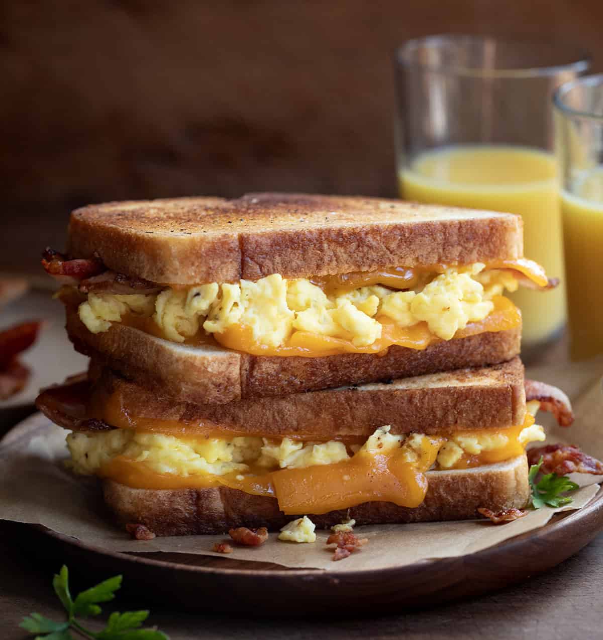 Stacked Griddle Breakfast Sandwich on s wooden plate with glasses of orange juice in the background.