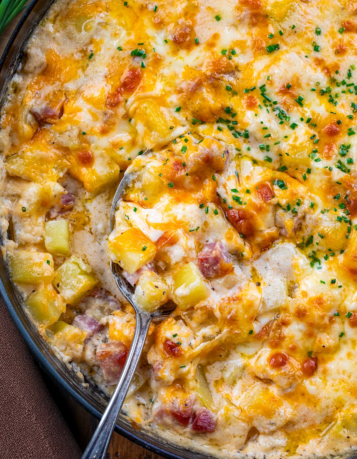 Spoon resting in a skillet of Ham and Potato Casserole.