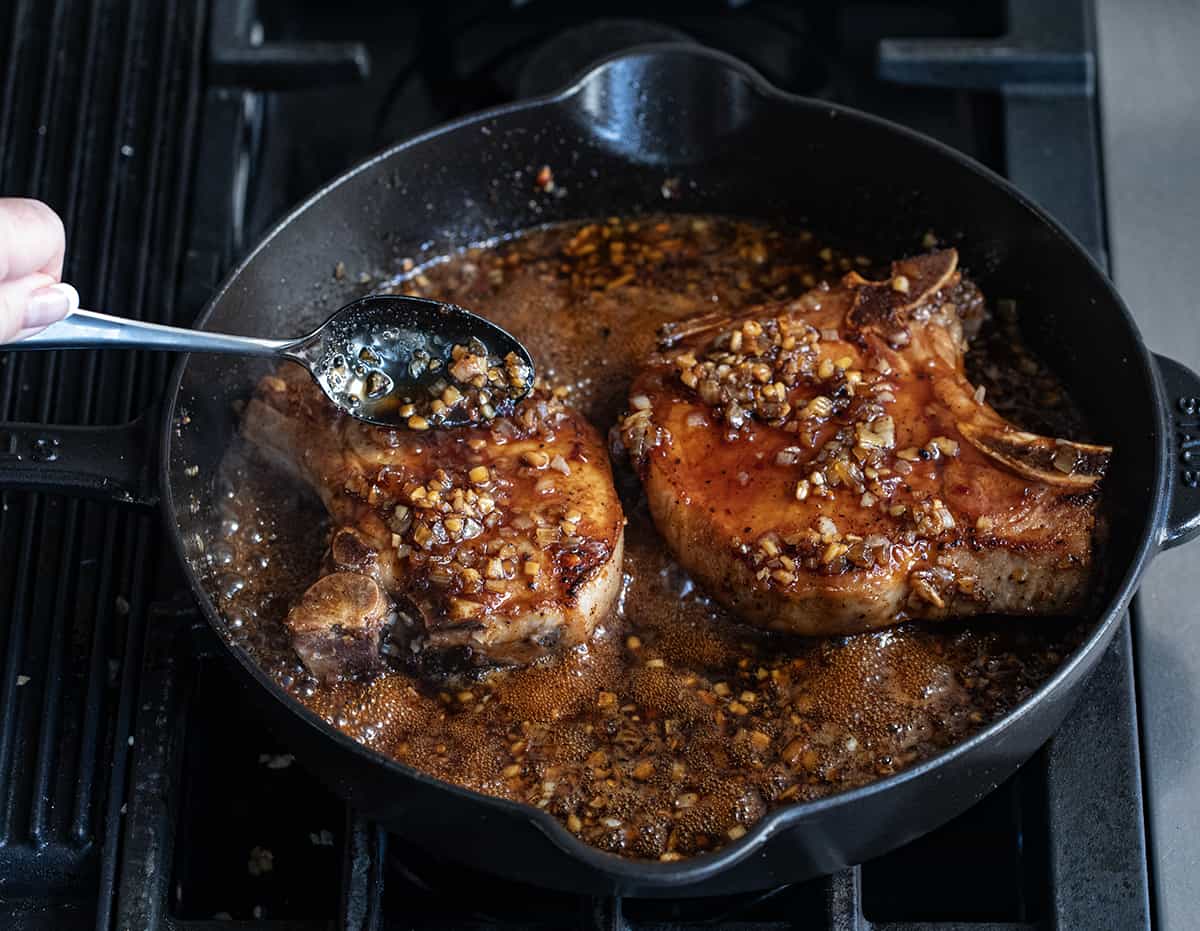 Spooning sauce over pork chops in a pan to make Honey Garlic Pork Chops.