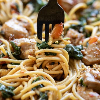 Fork Twirling Noodles in a Skillet of Tomato Spinach Chicken Spaghetti.