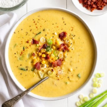 Bowl of Zucchini Chowder on a white table with bacon and scallions.
