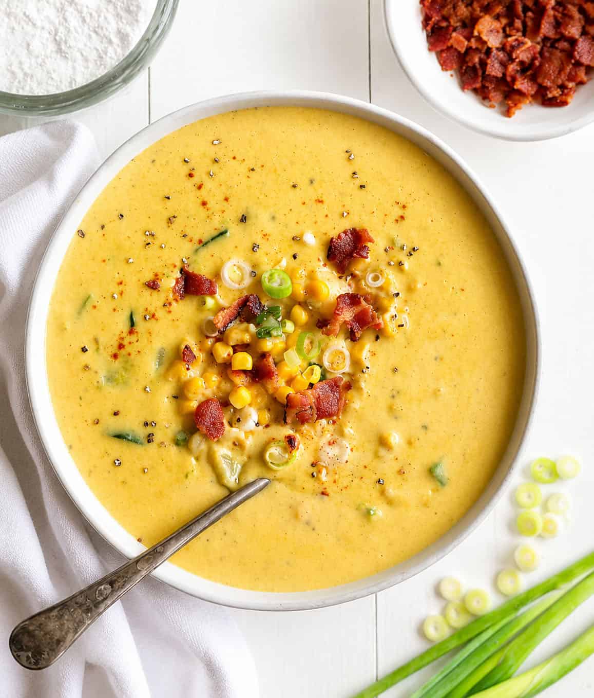 Zucchini Corn Chowder on a white table Bowl of Zucchini Chowder on a white table with bacon and scallions.