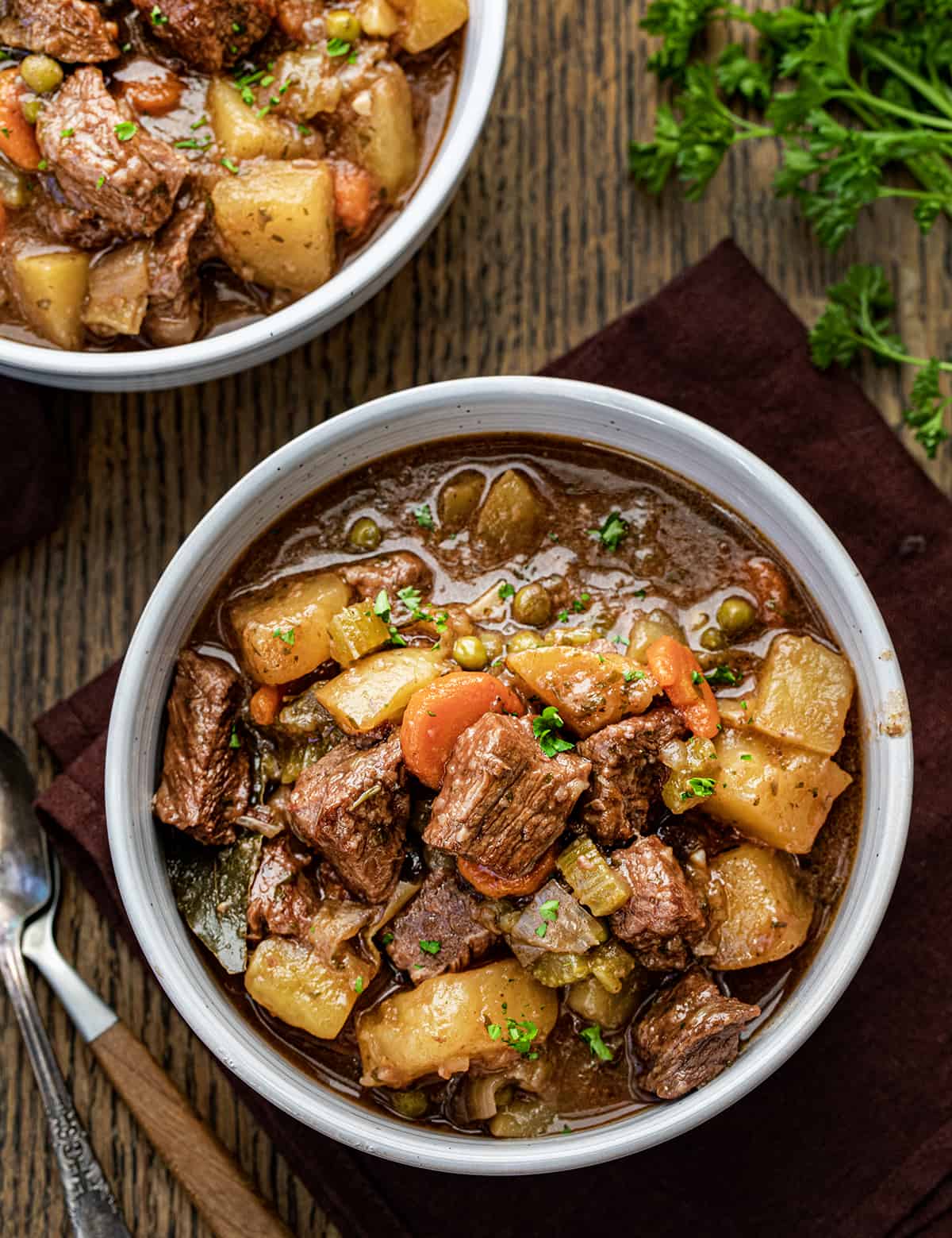 Two bowls of beef stew on a table with spoons and napkins.