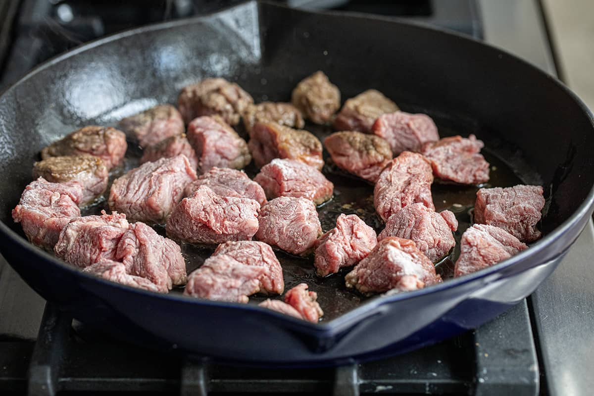 Beef pieces coated in flour searing in a hot skillet.