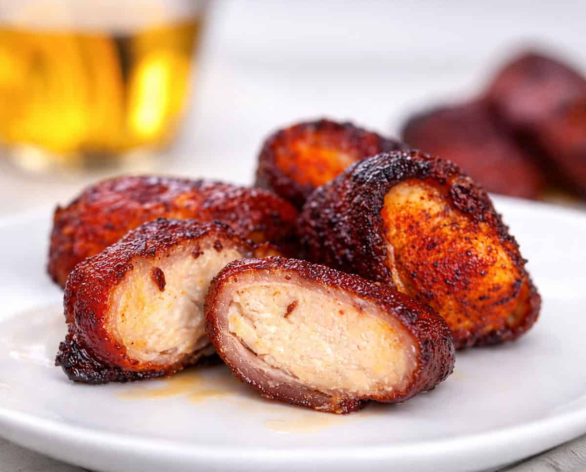 Bacon-Wrapped Chicken Bites on a white plate with beer in the background.