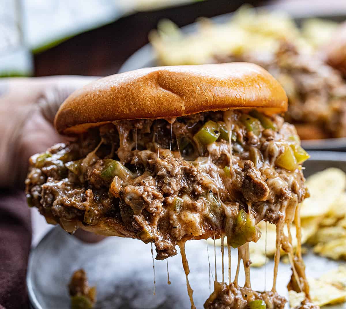 Hand Holding a Messy Philly Cheesesteak Sloppy Joe Sandwich.