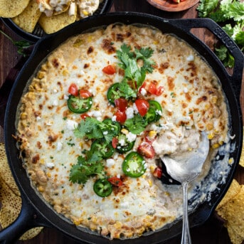 Skillet of White Bean Chili Cheese Dip on a Dark Table with a Spoon in it From Overhead.