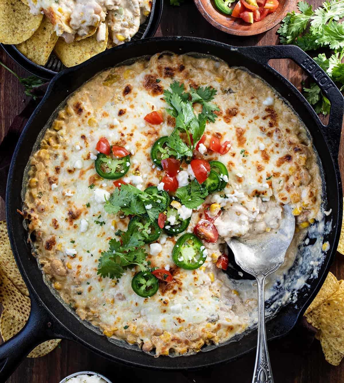 Skillet of White Bean Chili Cheese Dip on a Dark Table with a Spoon in it From Overhead. 