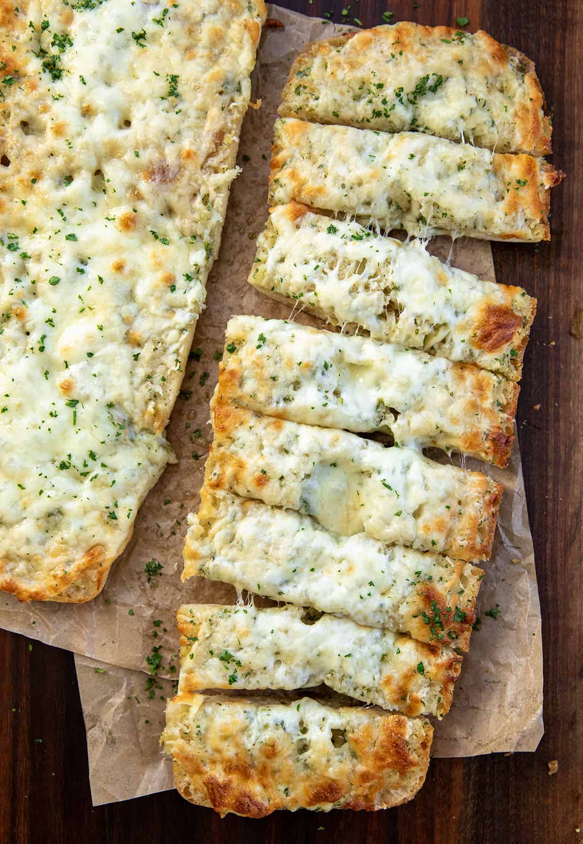 Garlic Cheese Bread on parchment paper with one of the half loaves cut into slices. 