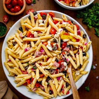 Serving bowl of Italian Pasta Salad with a spoon in it on a wooden table.