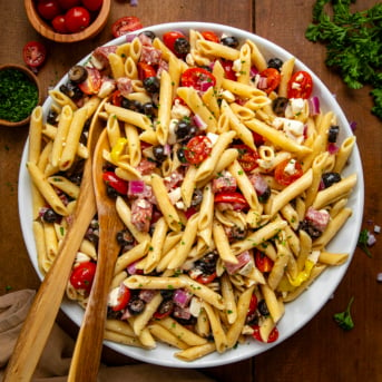 Serving bowl of Italian Pasta Salad with 2 wooden spoons on a wooden table from overhead.