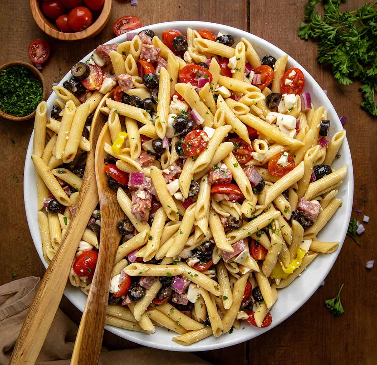 Serving bowl of Italian Pasta Salad with 2 wooden spoons on a wooden table from overhead. 