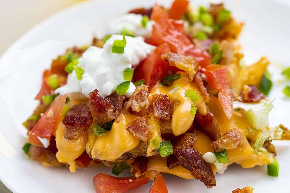 Close up of Waffle Fry Nachos Covered in Cheese and Toppings on White Plate