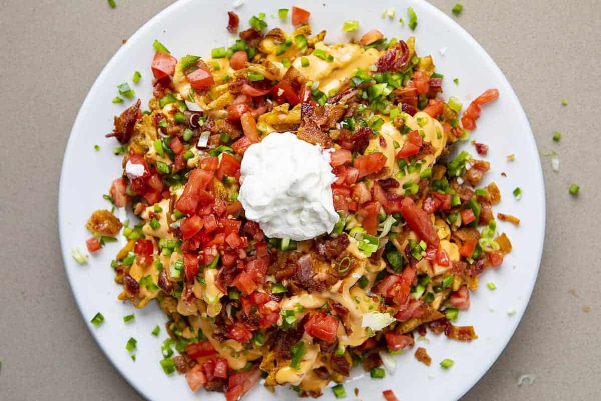 Overhead view of Waffle Fry Nachos with Toppings and Sour Cream on White Plate
