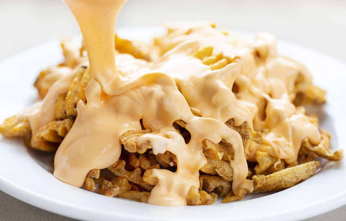 Pouring Cheese Sauce over Waffle Fry Nachos