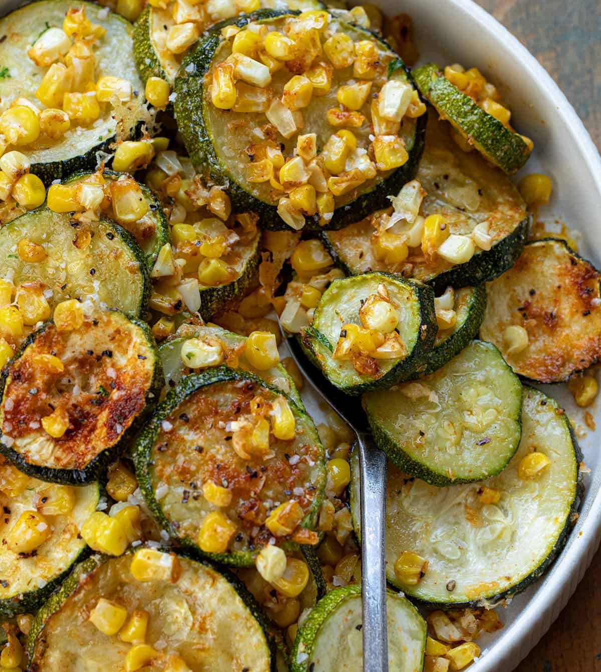 CLose up of a bowl with Roasted Zucchini and Corn in it and with a spoon.