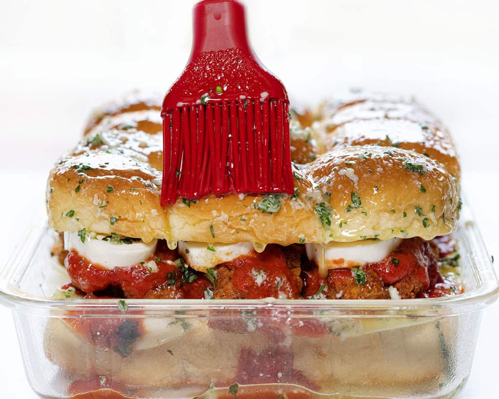 Sliders are one of the easiest ways to feed a crowd. They’re fun, customizable, and perfect for parties, game days, holidays, and family dinners! Chicken Parmesan Sliders in a glass pan with garlic butter being brushed on.