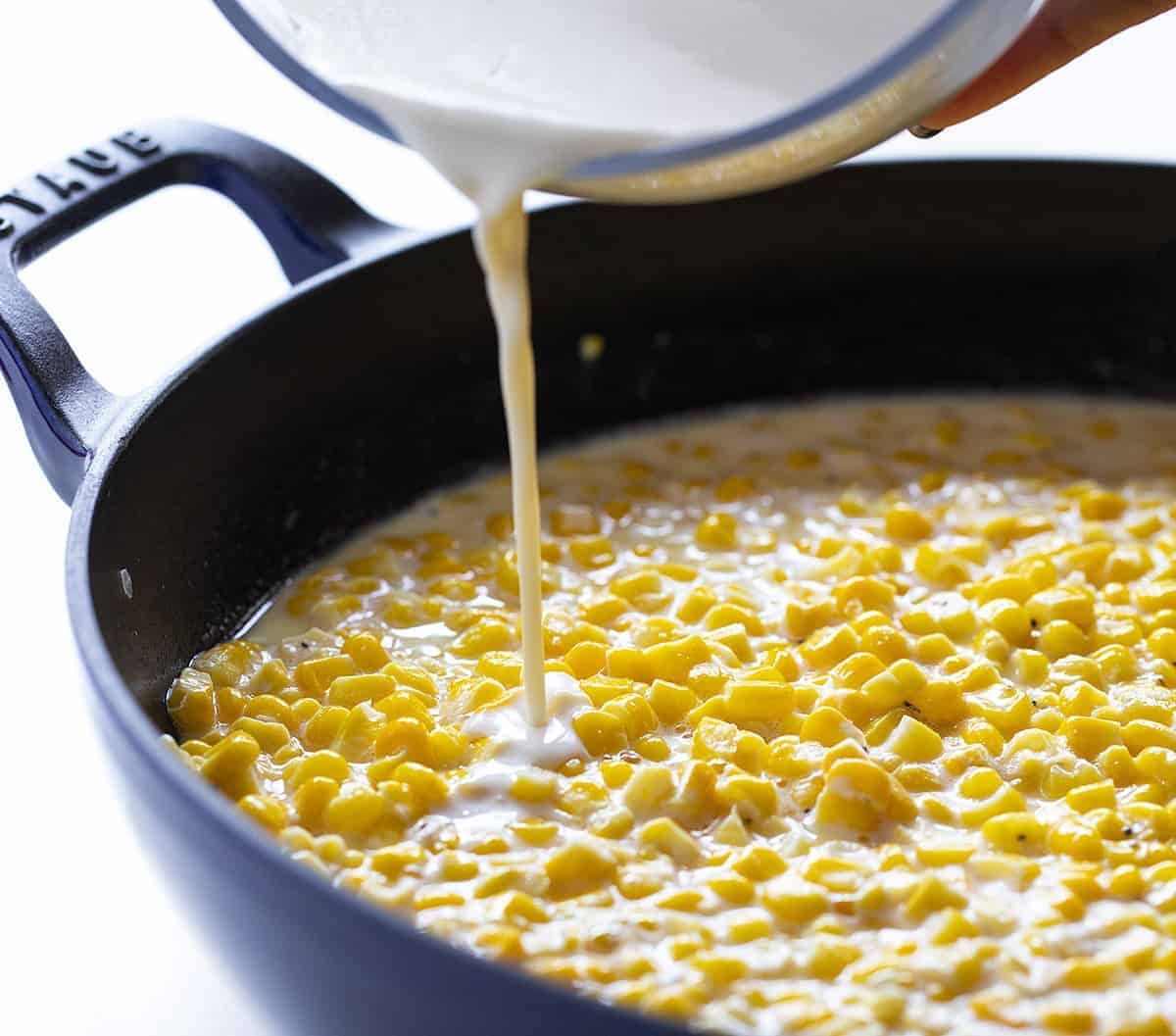 Cream being poured into a pan of corn
