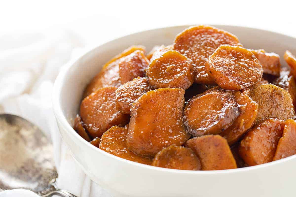 Bowl of Candied Yams Sprinkled with Flakey Salt and Next to a Serving Spoon. 