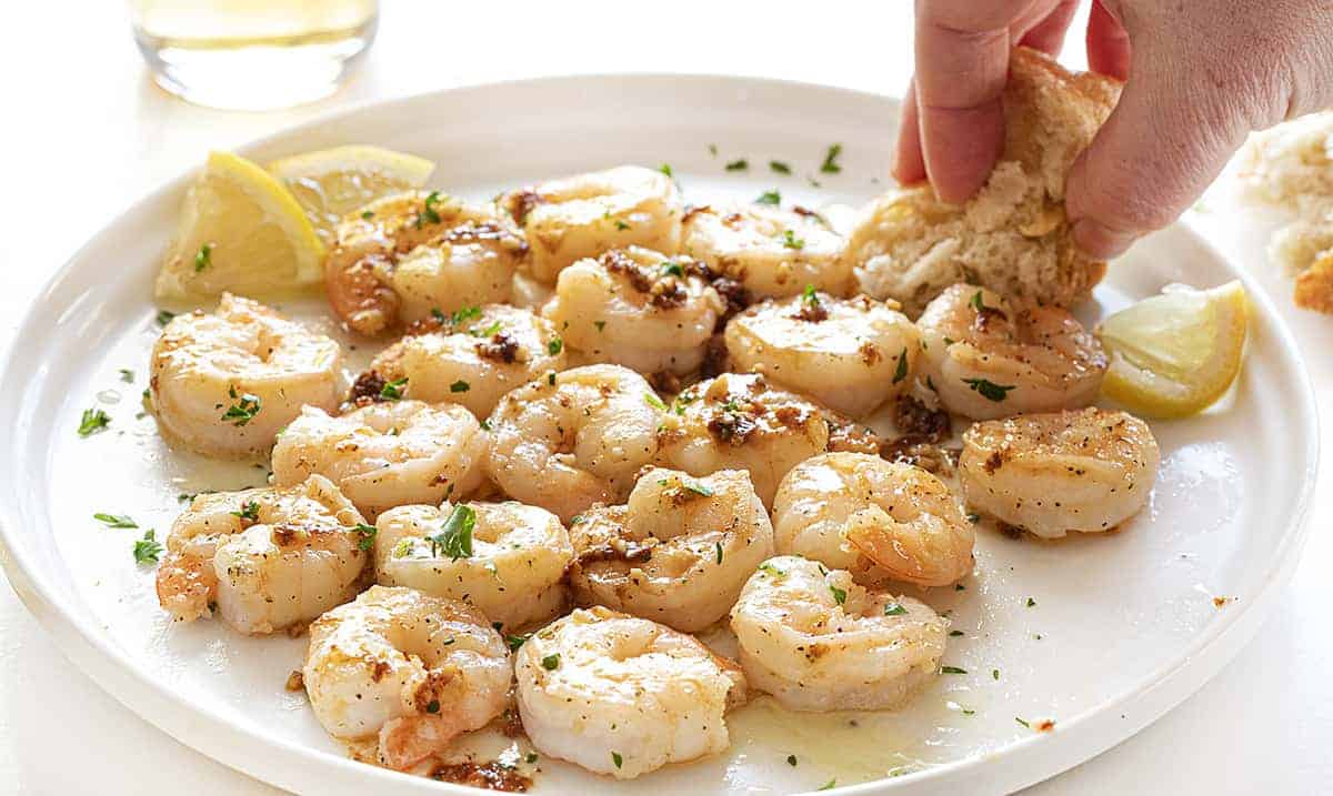Dipping Bread into Shrimp Scampi on a White Plate