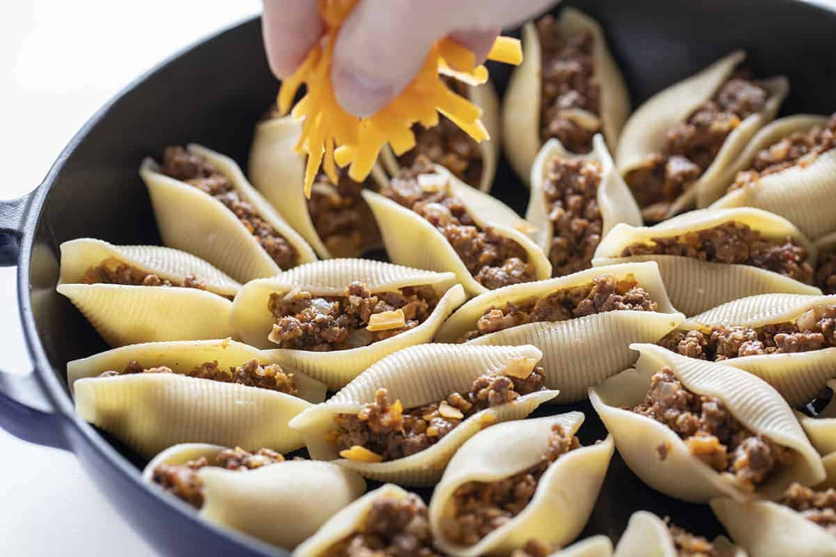 Sprinkling Cheddar Cheese over Cheeseburger Stuffed Shells