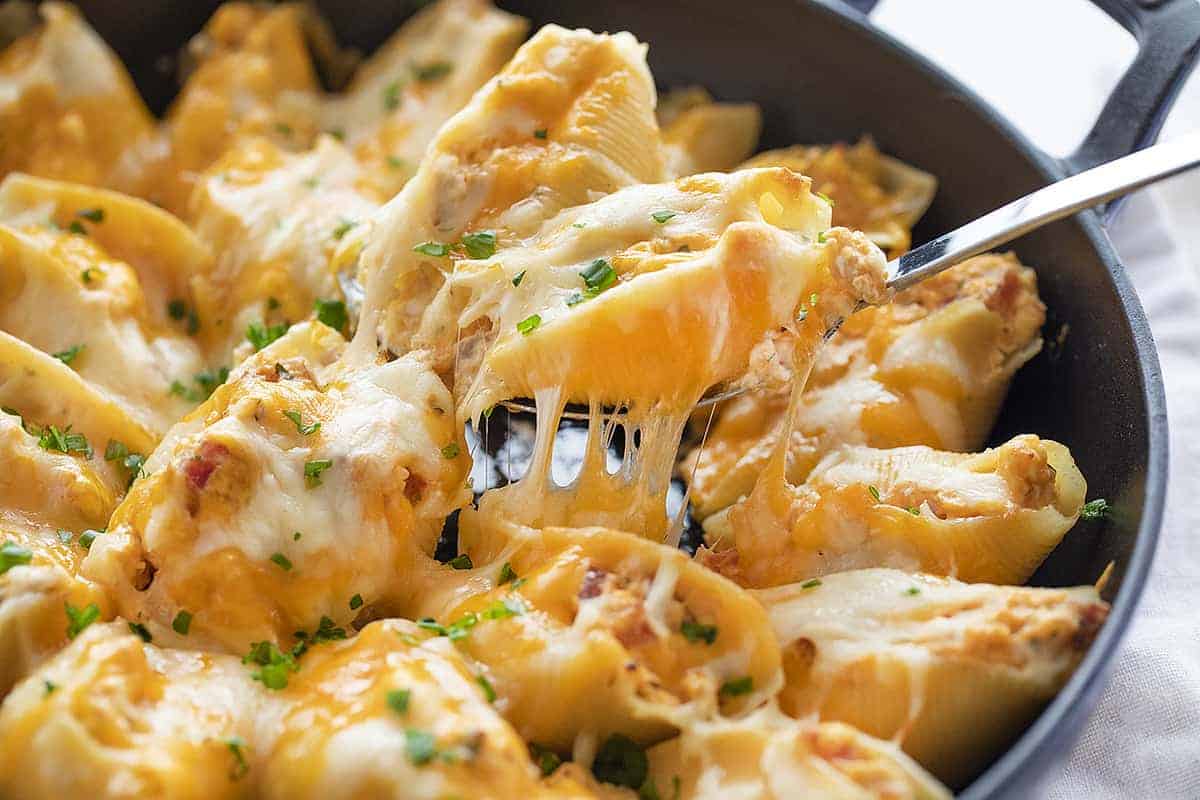 Cheesy Chicken Bacon Ranch Stuffed Shells Being Lifted Out of Skillet