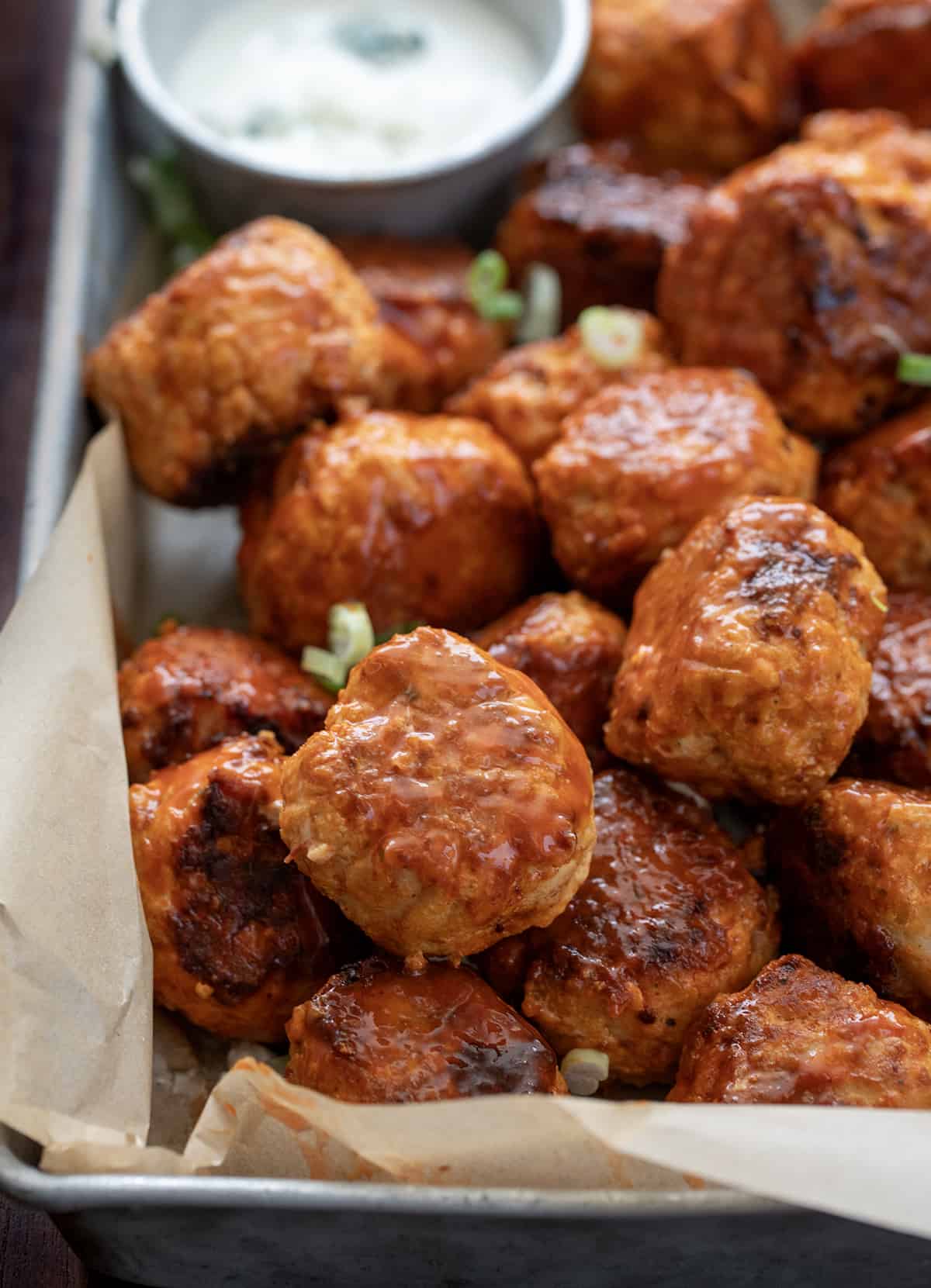 Close up of Buffalo Chicken Meatballs in a Pan with Blue Cheese Dressing Behind.
