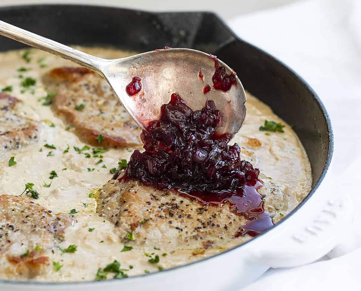 Spooning Cherry Sauce over Pork Chips in Skillet with Cream Cheese Sauce