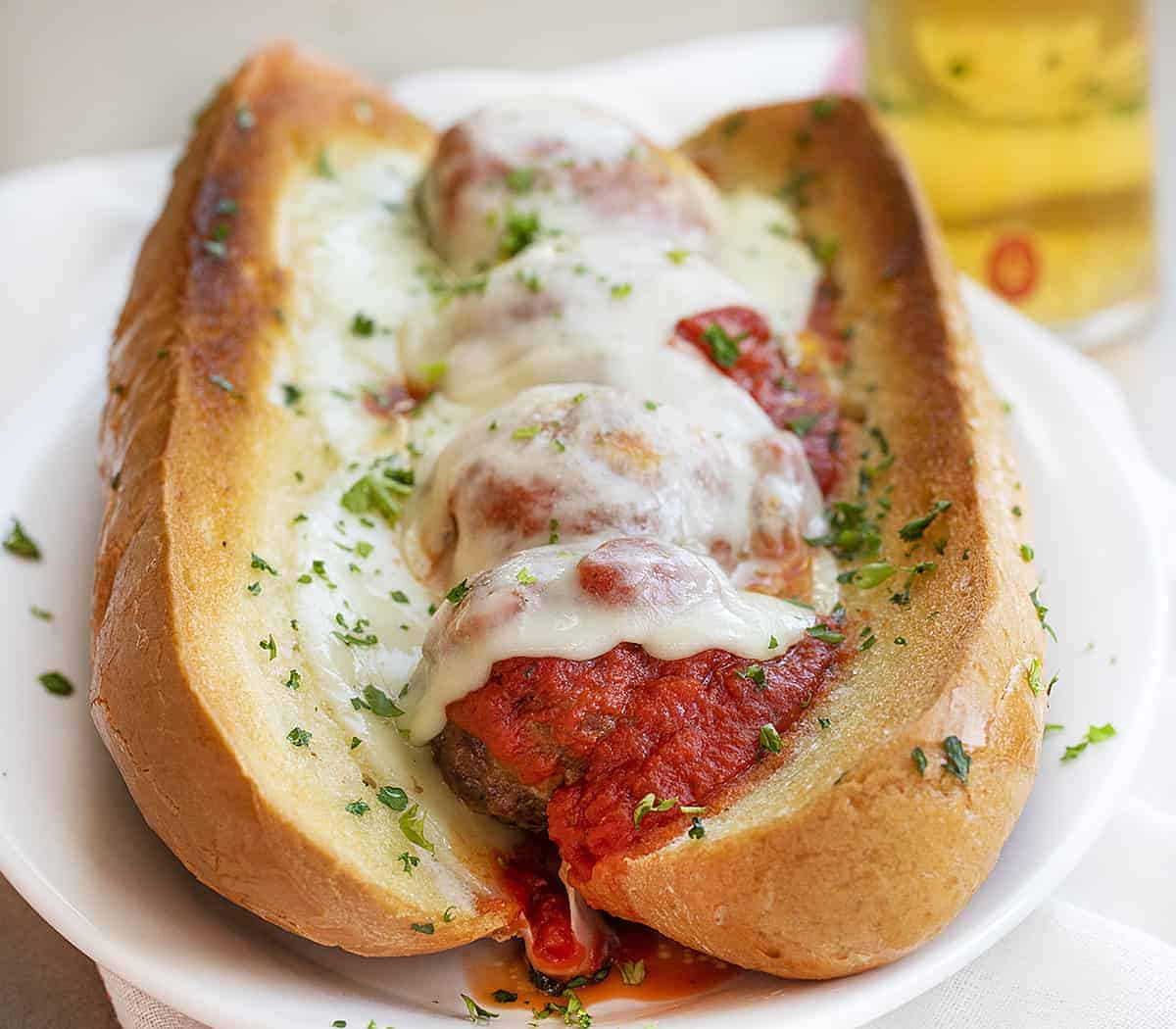 Cheese Stuffed Meatball Sub on a White Plate with Beer in Background