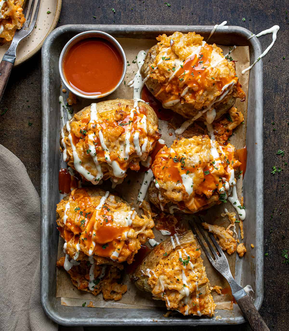 Overhead Image of Buffalo Chicken Twice Baked Potatoes on a Pan with Sauce and One Potato has been Cut in half.