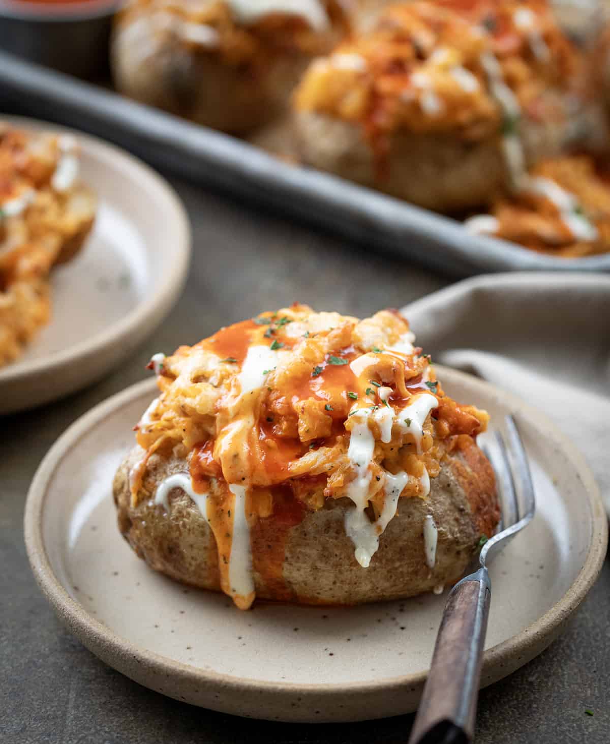 One Buffalo Chicken Twice Baked Potato on a Plate with. fork with More in the Background.