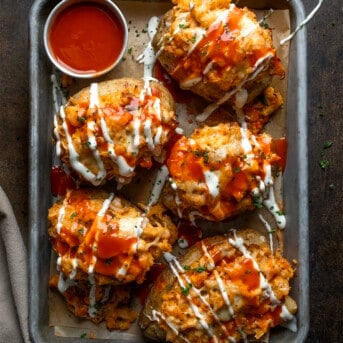 Buffalo Chicken Twice Baked Potatoes in a Pan with Sauce Fully Drizzled in Sauces and Shot from Overhead.