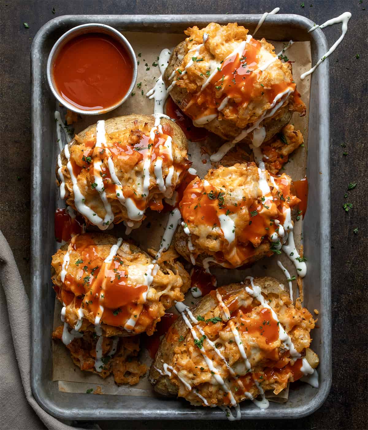 Buffalo Chicken Twice Baked Potatoes in a Pan with Sauce Fully Drizzled in Sauces and Shot from Overhead.
